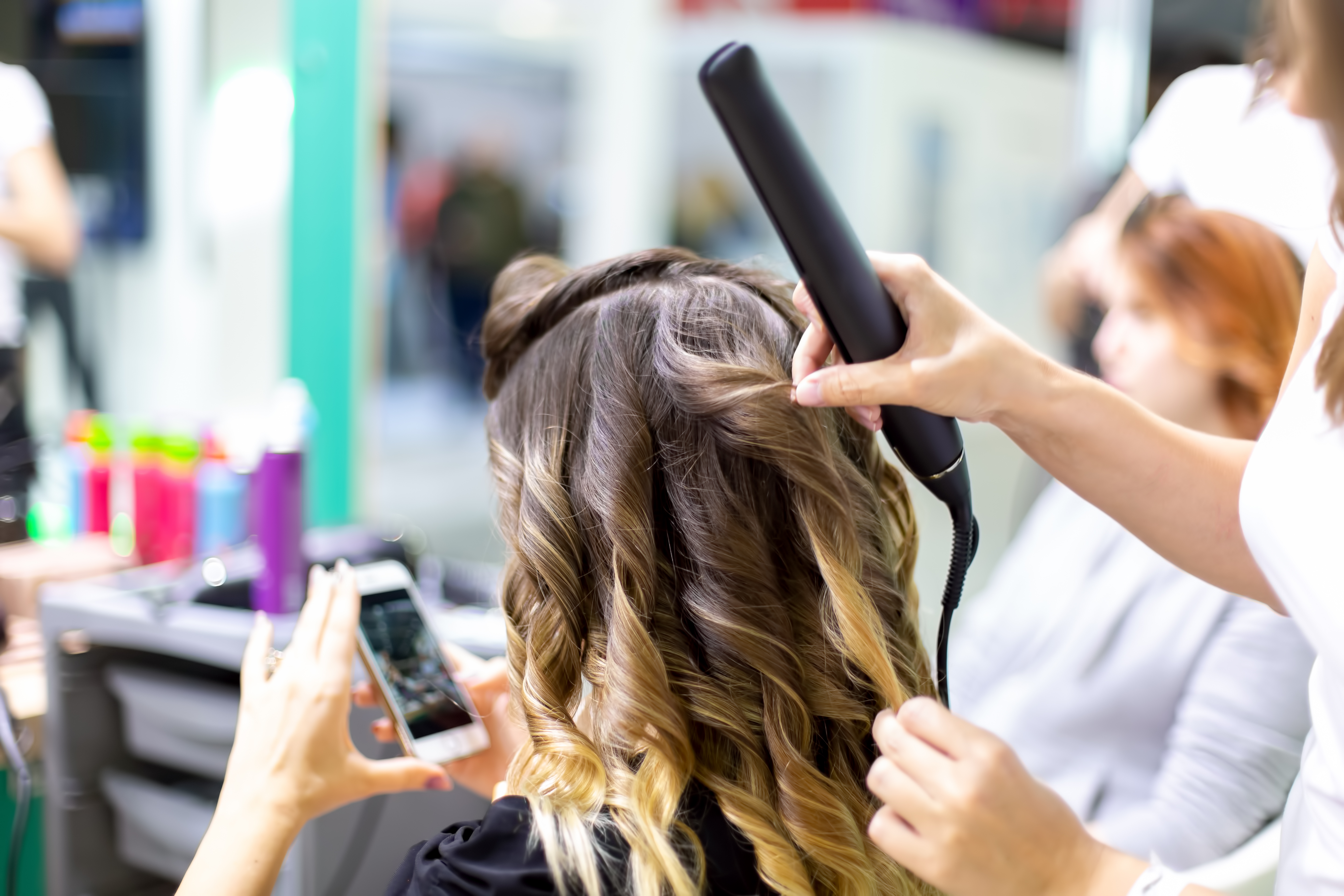 close up stylist makes girl client styling hair waving with curling irons hairdresser