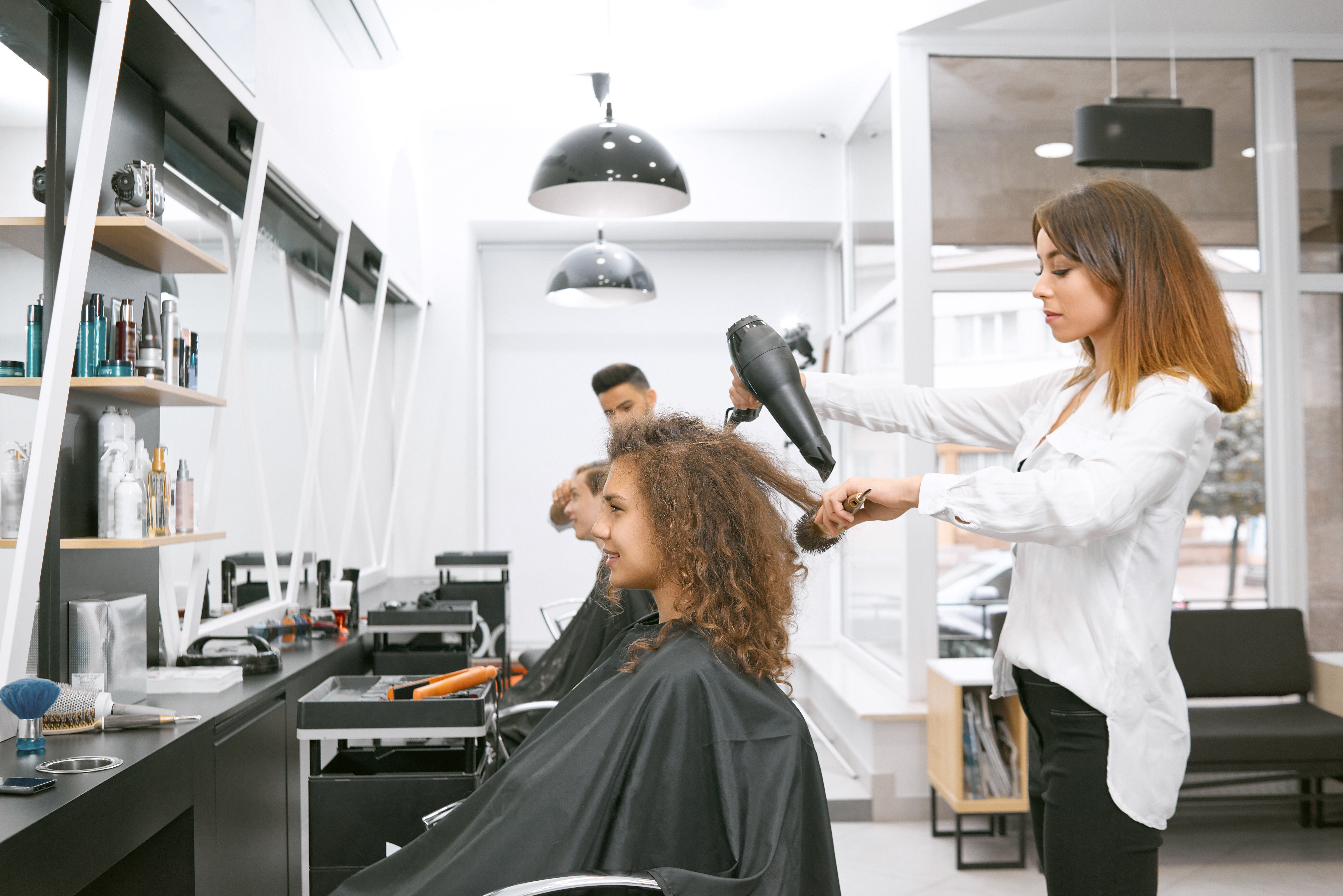 female hairstylist drying curly girl s hair using big plastic brush